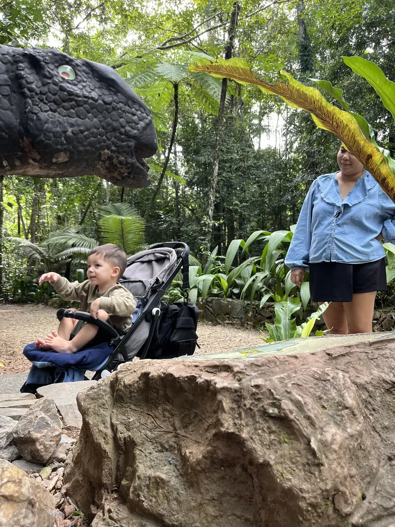A toddler in a stroller beside a dinosaur model on the trail