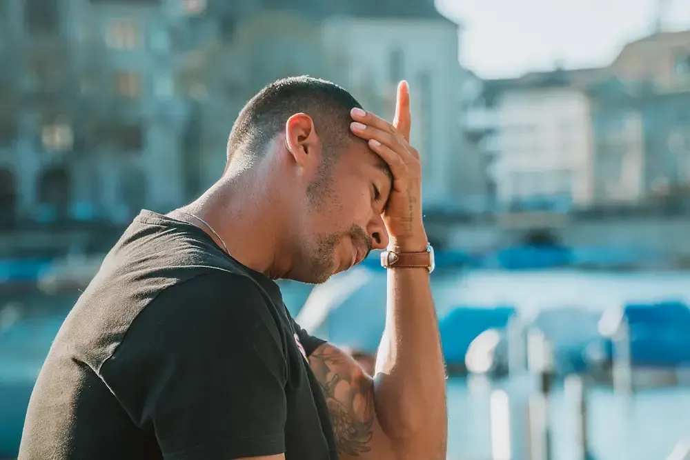 A stressed man holding his forehead by the water