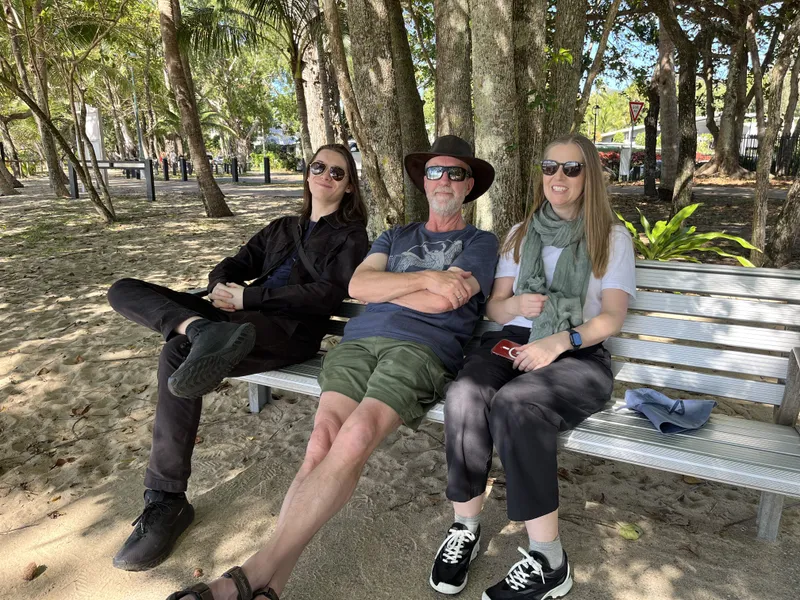 Three people relaxing on a bench under the trees