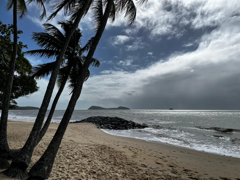 Leaning palms over the beach, with a rock wall and islands offshore