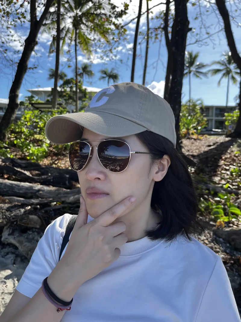A woman in a cap and sunglasses under the casuarinas