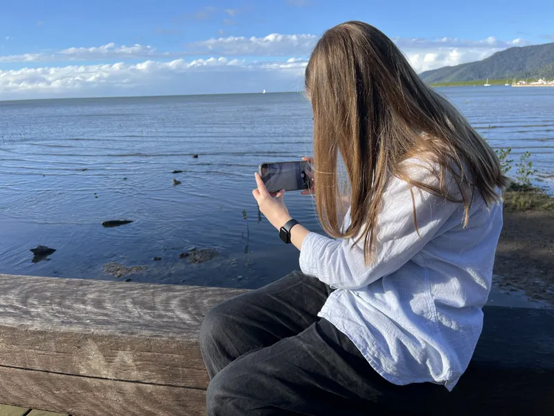 A woman sitting on the timber railing photographing the inlet