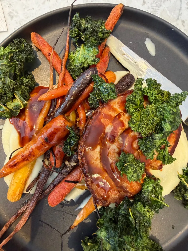 A plate of roasted heirloom carrots and crispy kale over mash with a rich glaze