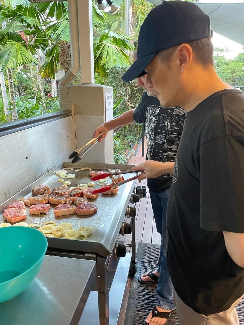 Two men cooking steaks and onions on the flat-top barbecue