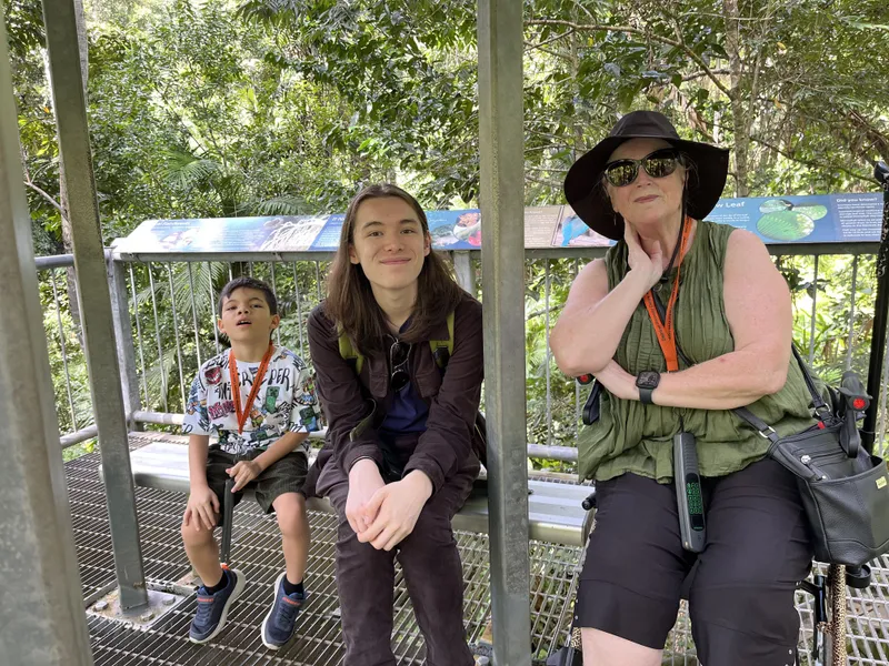 A boy, a teenager and a woman sitting on a bench in the forest