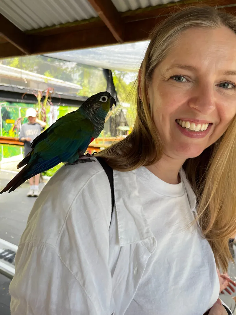 A woman smiling with a parrot on her shoulder