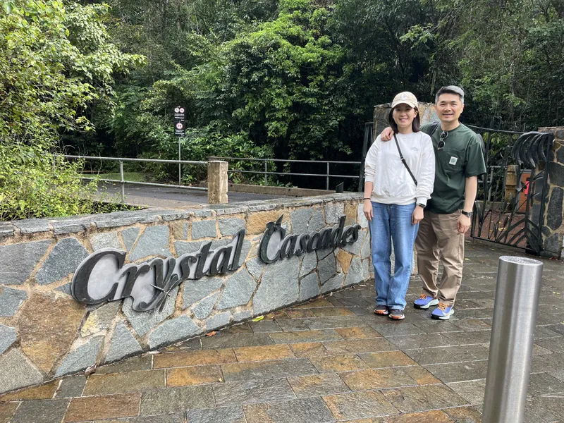 Cris and Khon by the Crystal Cascades sign, with the rainforest behind