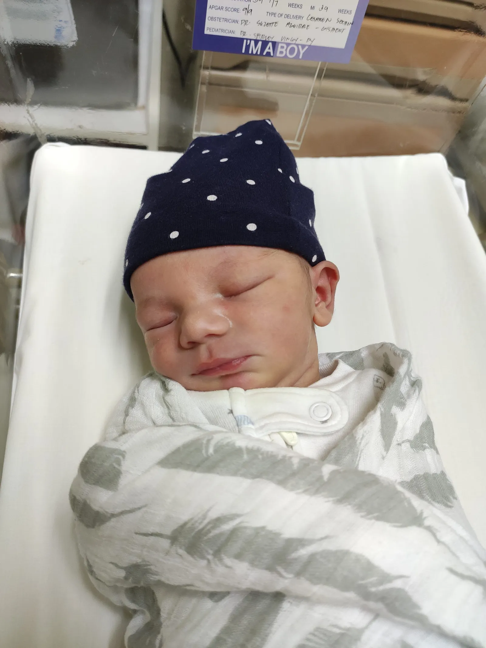 Newborn Jaxon asleep in a hospital bassinet, wearing a beanie