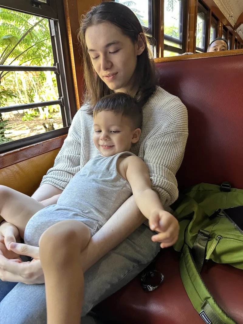 The toddler pointing out of the window from the teenager's lap