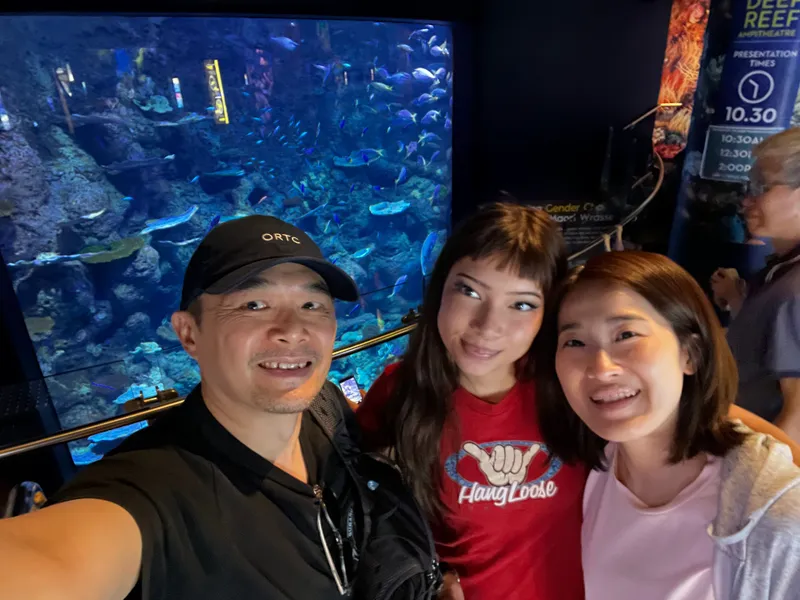 A selfie of three people in front of a big reef tank