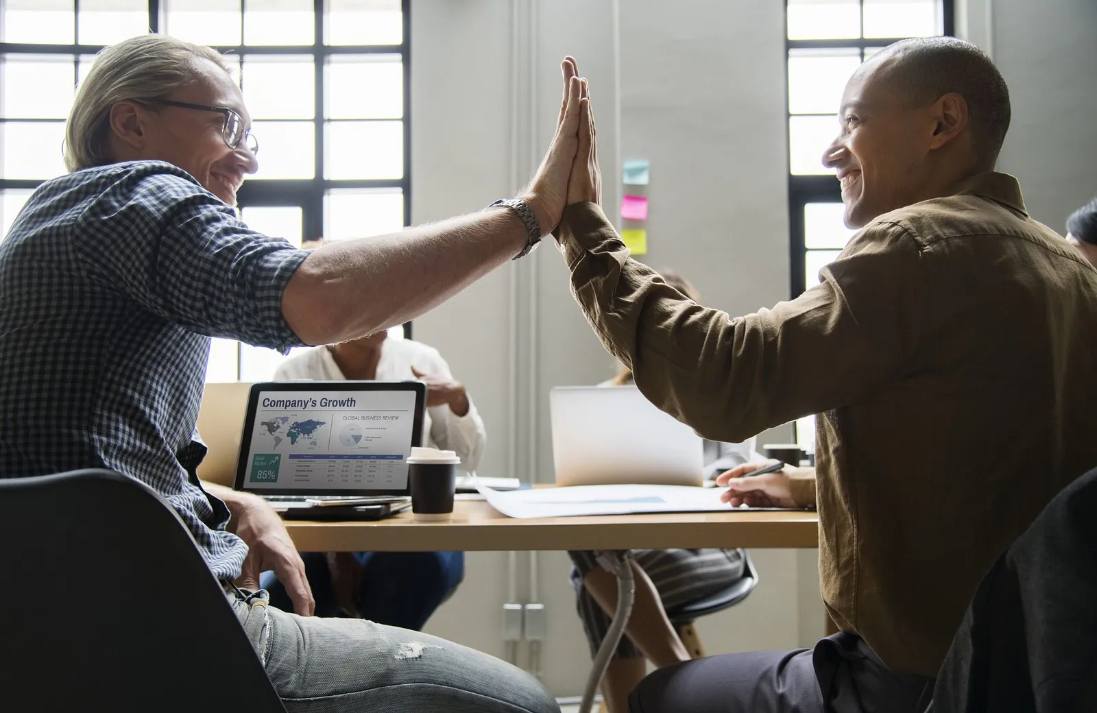 Two colleagues high-fiving across a desk in an office