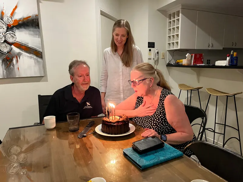 Steve and Lin at the table with a lit birthday cake, Lin about to blow out the candles