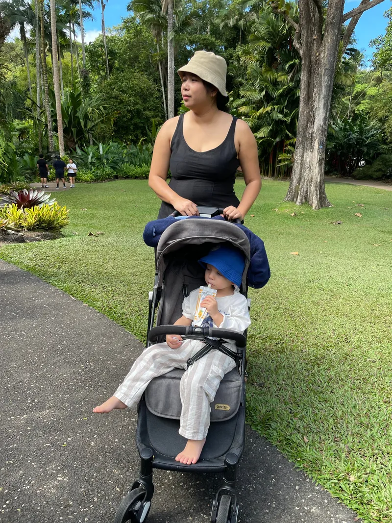 A woman pushing a toddler in a stroller along a garden path