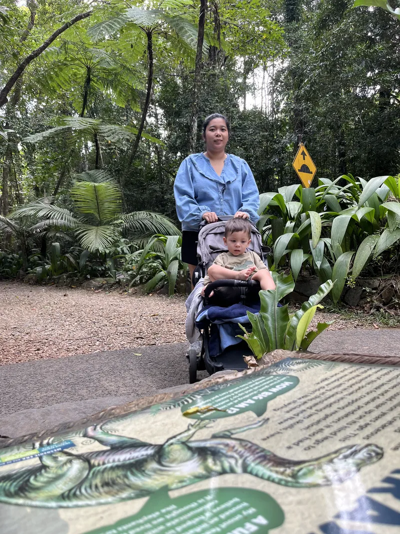 A woman pushing the toddler in the stroller along the path