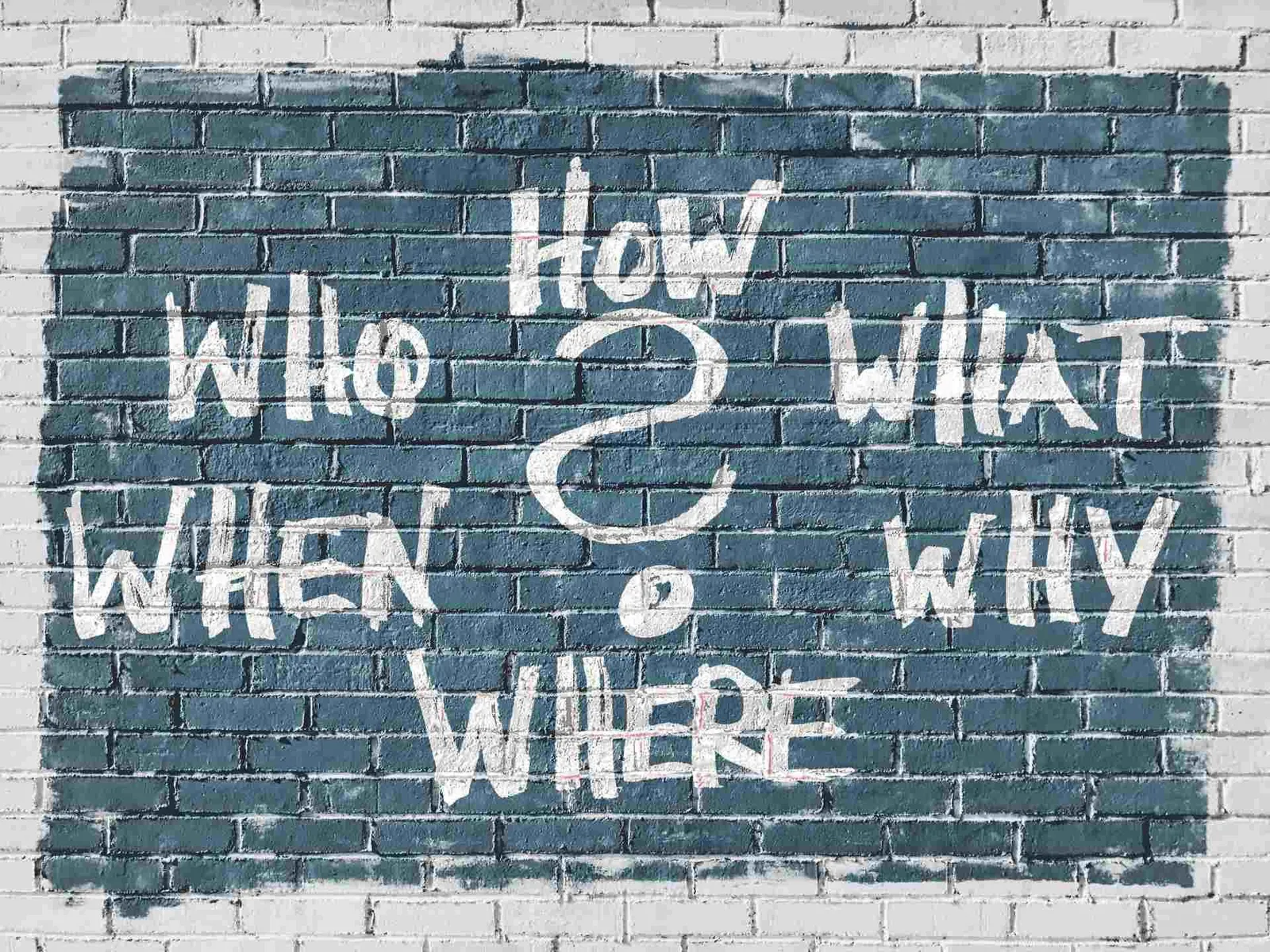 Who, what, when, where, why and how written in chalk on a brick wall