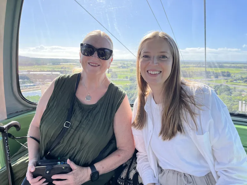 Two women smiling in a gondola, with the coastal plain far below