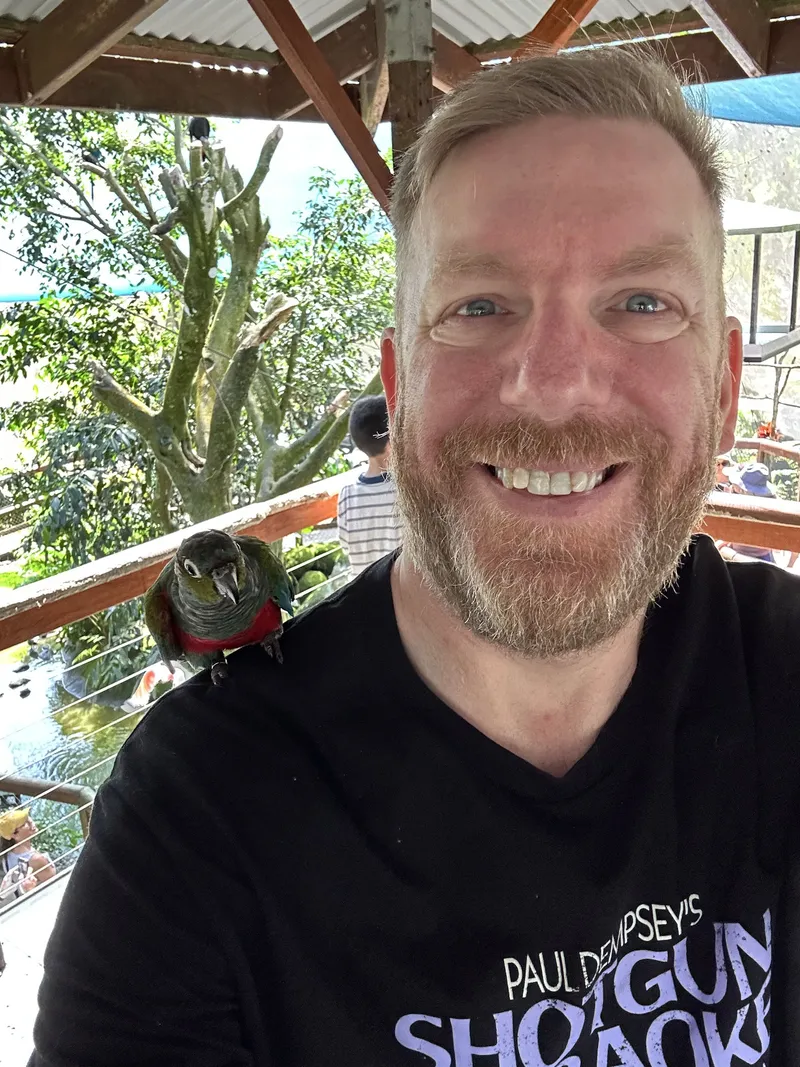 A selfie of a man with a parrot on his shoulder