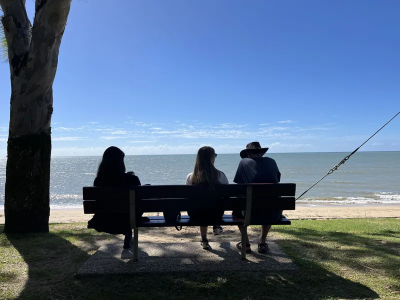 Three people on a bench by the sea, in silhouette