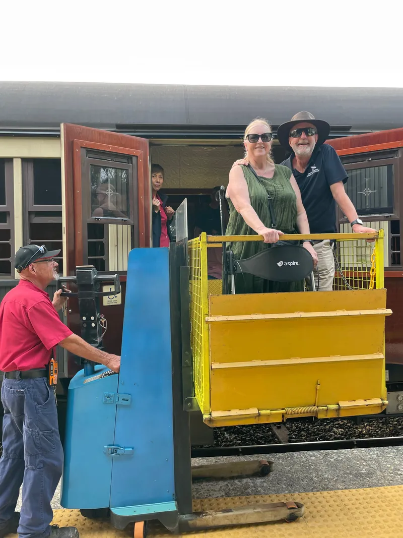 A woman and a man in a bush hat on a lift beside the train