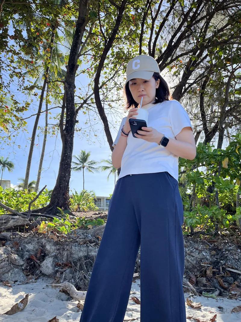 A woman sipping a drink under the trees at the back of the beach