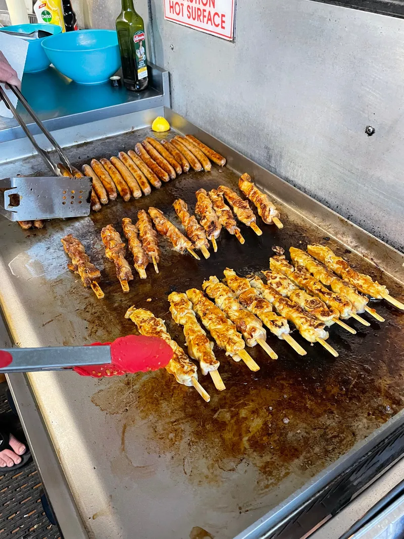 Chicken skewers and sausages sizzling on the flat-top