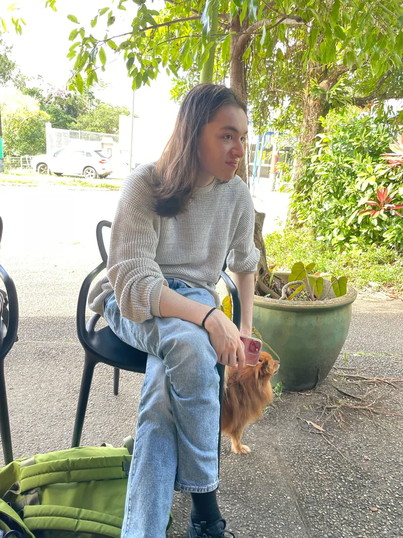 A teenager sitting outside the cafe, a small dog beside the chair