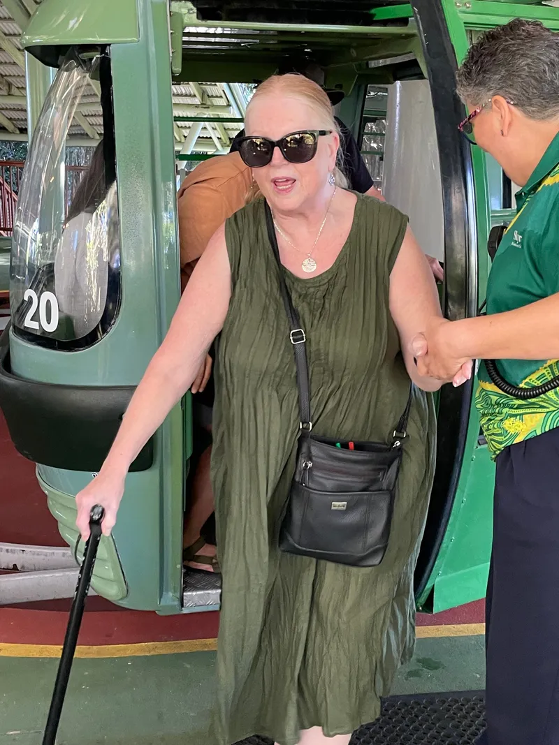 A woman with a cane stepping out of the gondola with help from staff