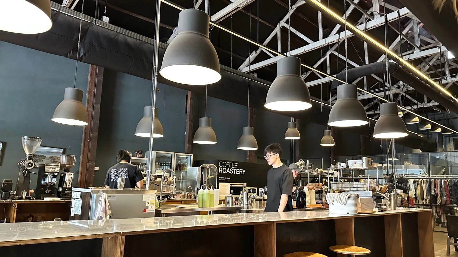 Baristas behind the long bar of a warehouse coffee roastery in Bangkok, under rows of pendant lights
