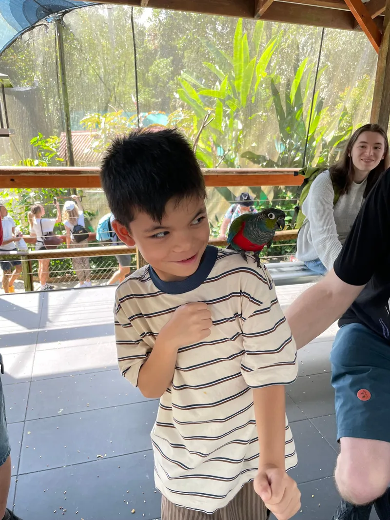 A boy grinning with a parrot on his shoulder