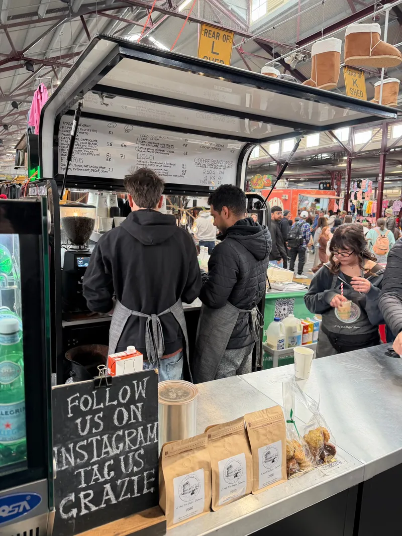 Baristas at a coffee cart in the busy market sheds, with Ugg boots hanging overhead
