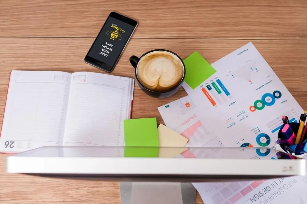 A desk with a notebook, coffee, phone and charts seen from above