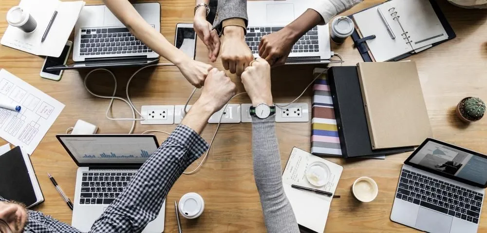 Hands meeting in a fist bump over a table of laptops