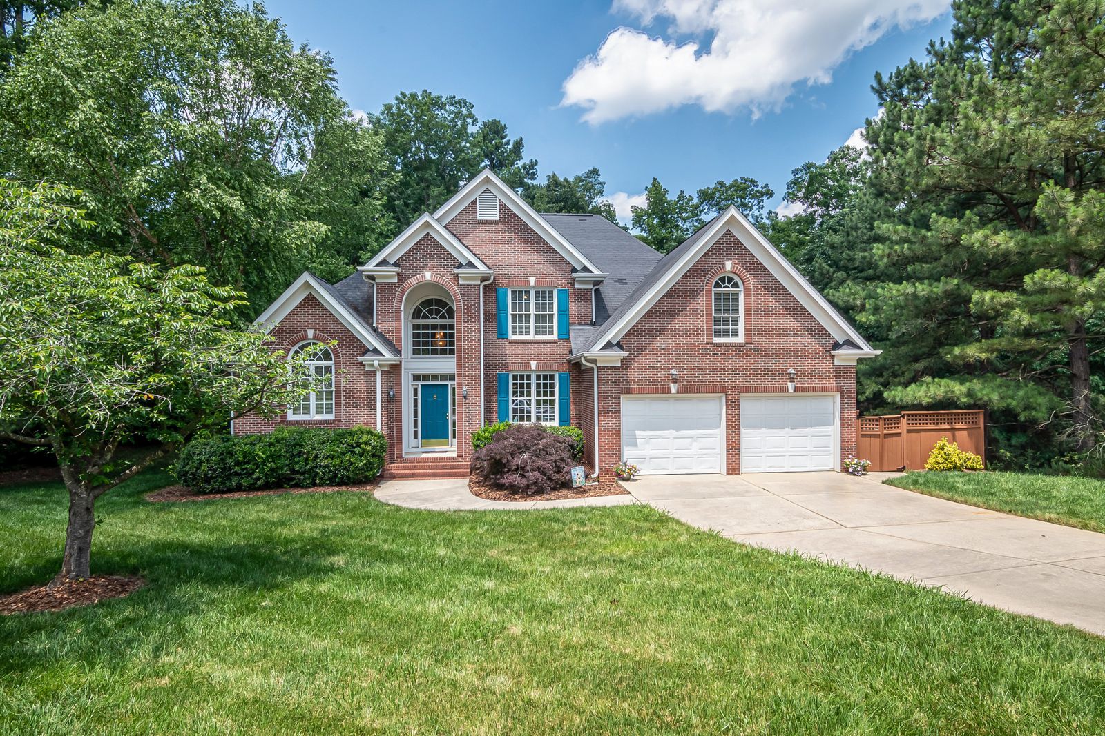 Two-story brick home with blue front door and landscaped lawn