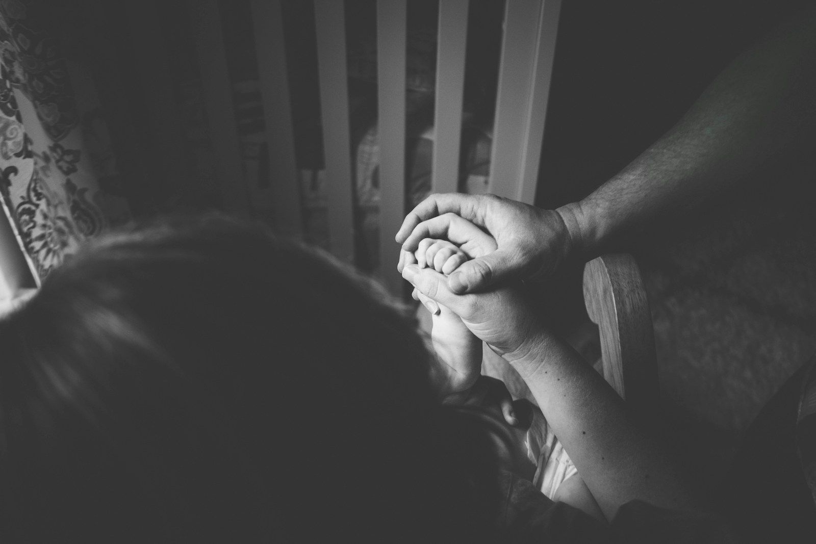 Black-and-white close-up of family hands holding a child's hand