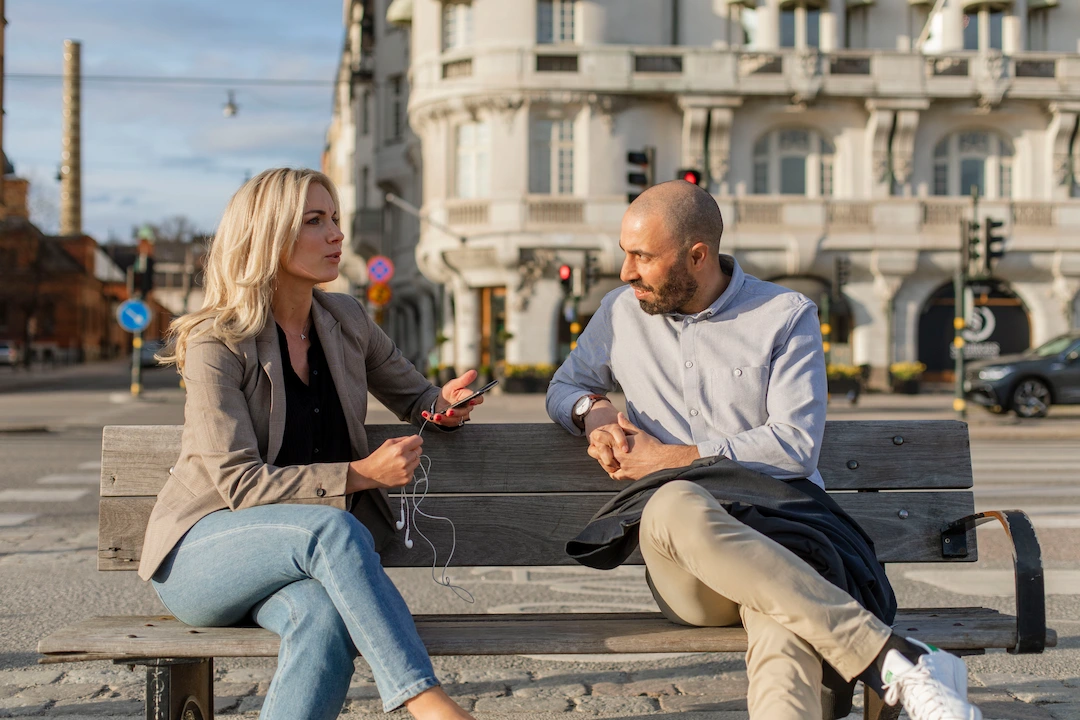 Två personer sitter bredvid varandra på en bänk i solen