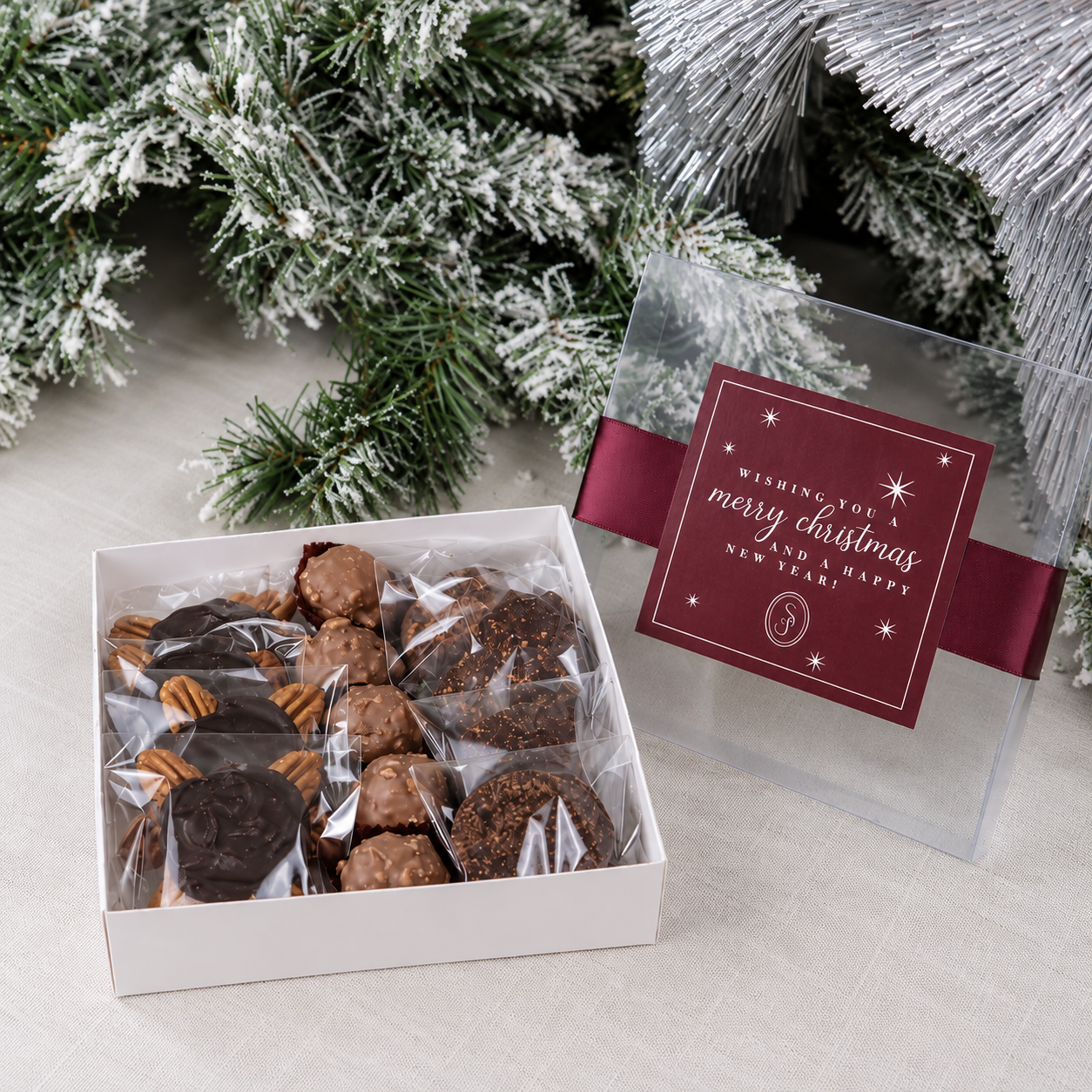 Caja navideña de regalo abierta con mix de chocolates artesanales y tapa transparente con lazo