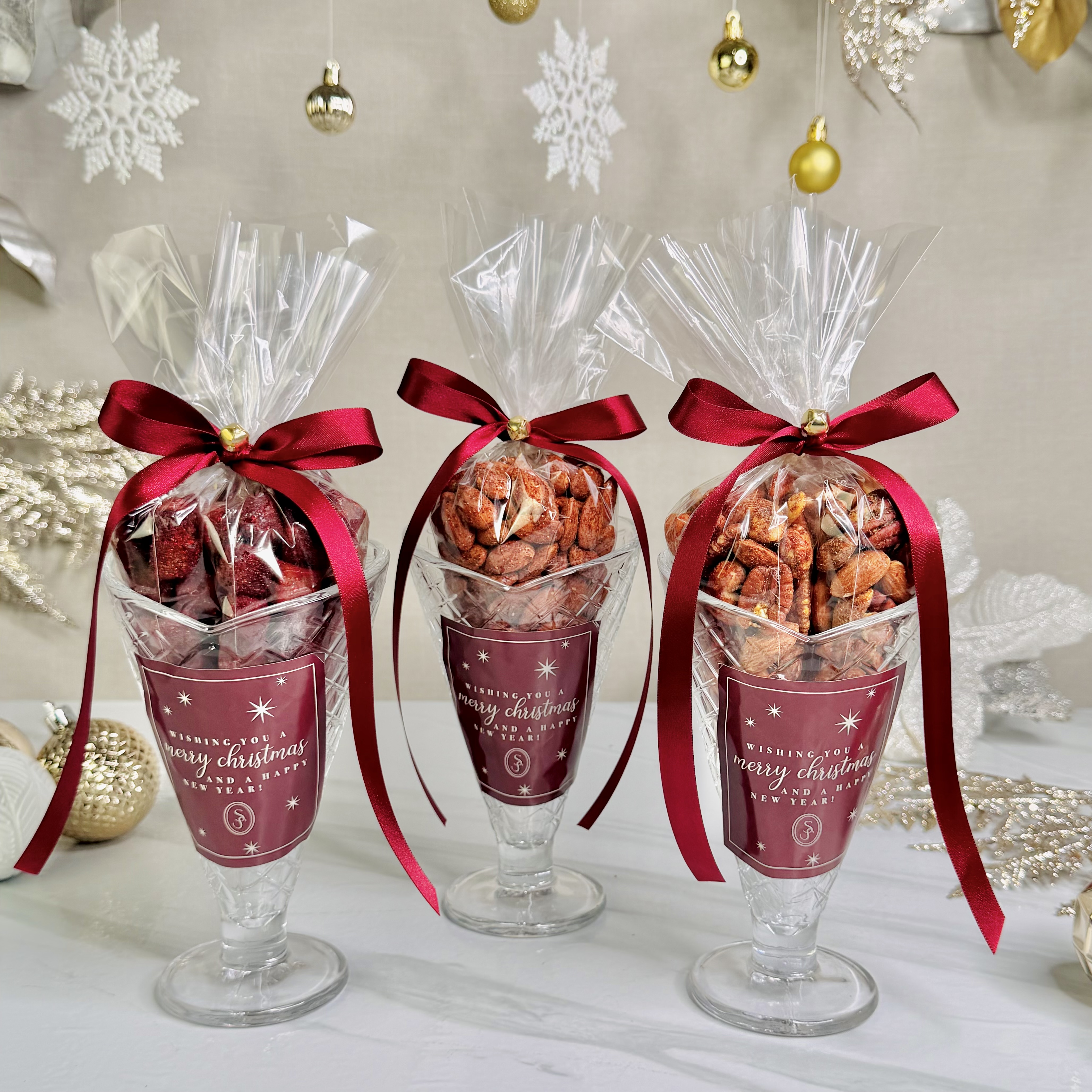 Copas triangulares de cristal con variedad de botanas, decoradas con moños rojos y presentación navideña
