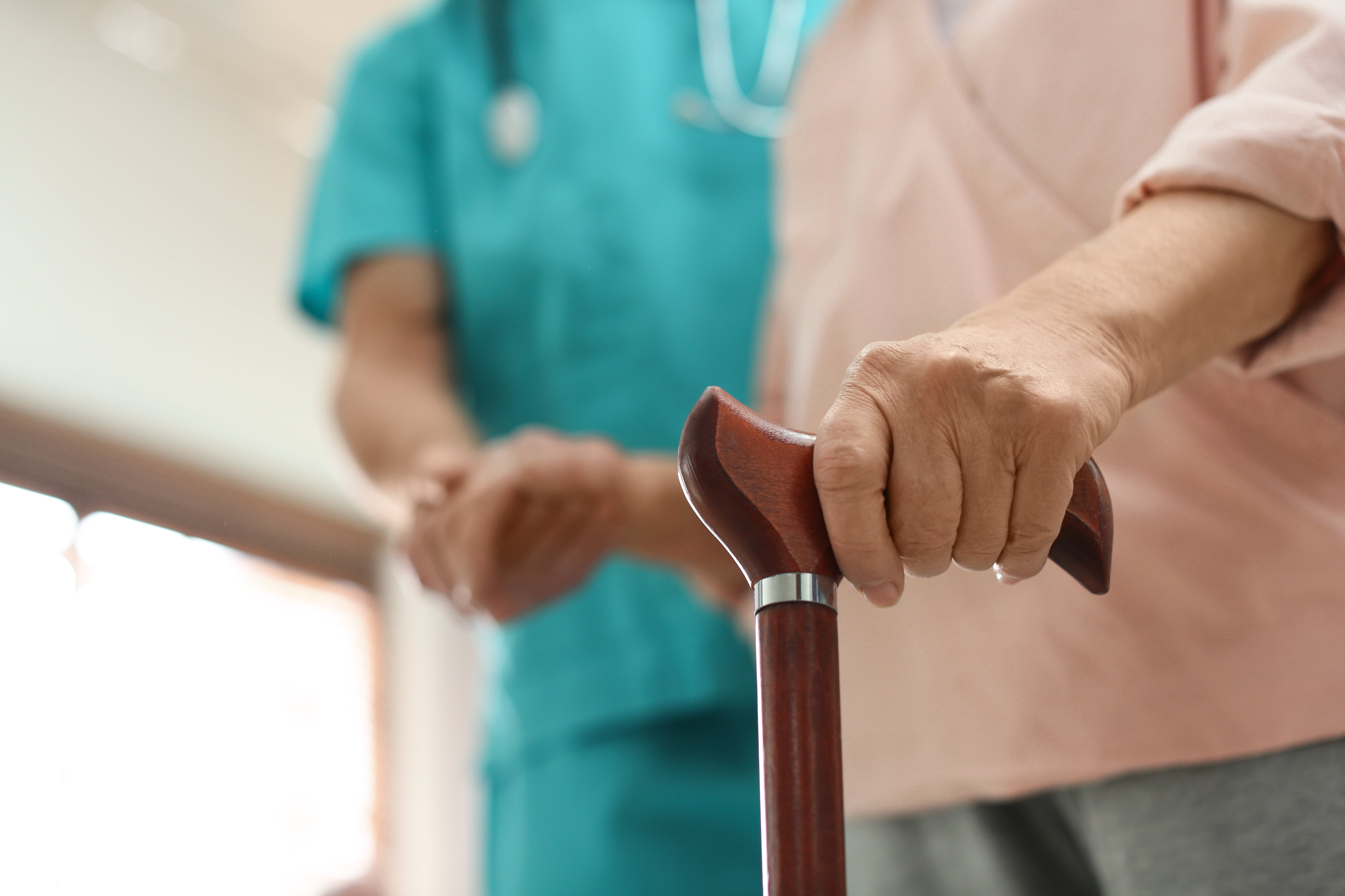 Femme atteinte de la maladie de Parkinson ayant des difficultés à marcher. Une aide soignante l'assiste pour avancer. 