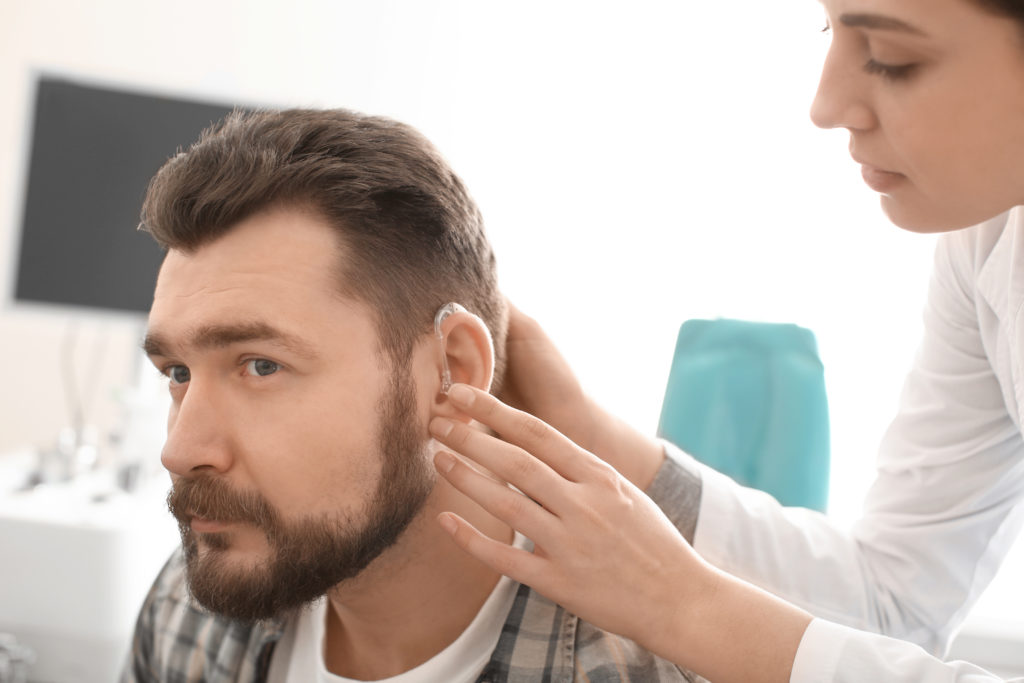 Otolaryngologist putting hearing aid in man's ear in hospital Cara Tepat Mengatasi Gangguan Pendengaran