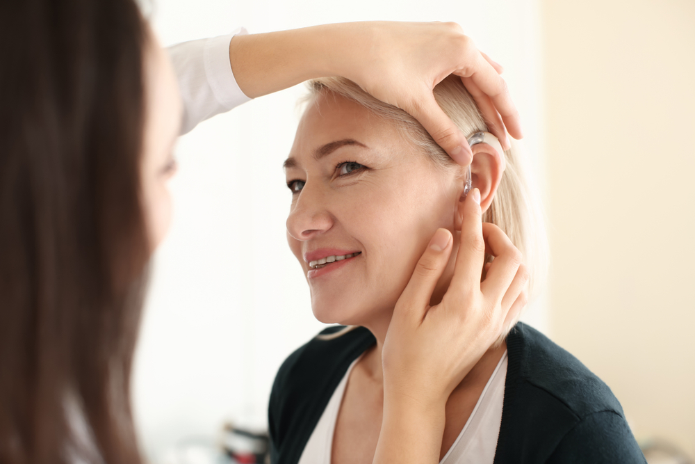 Otolaryngologist,Putting,Hearing,Aid,In,Woman's,Ear,On,Light,Background Tempat Terbaik Dan Cara Mendapatkan Alat Bantu Dengar