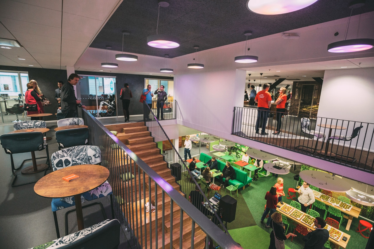 Ihmiset työskentelevät ja viettävät aikaa värikkäässä Werstaan Paratiisi‑tilassa, jossa on portaikko, vihreitä työalueita ja rento yhteisöllinen tunnelma.