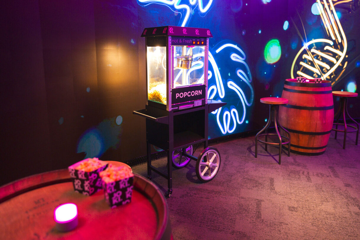 Popcornkone tapahtumatilassa, viereisellä tynnyripöydällä popcorn‑kupit ja tunnelmavalaistus.
