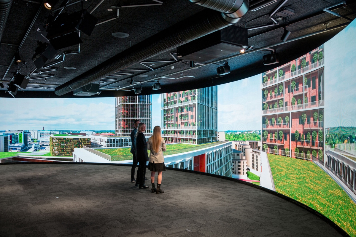 Kaksi ihmistä Joen Showroomissa, jossa on koko tilan levyinen kaareva led-näyttö