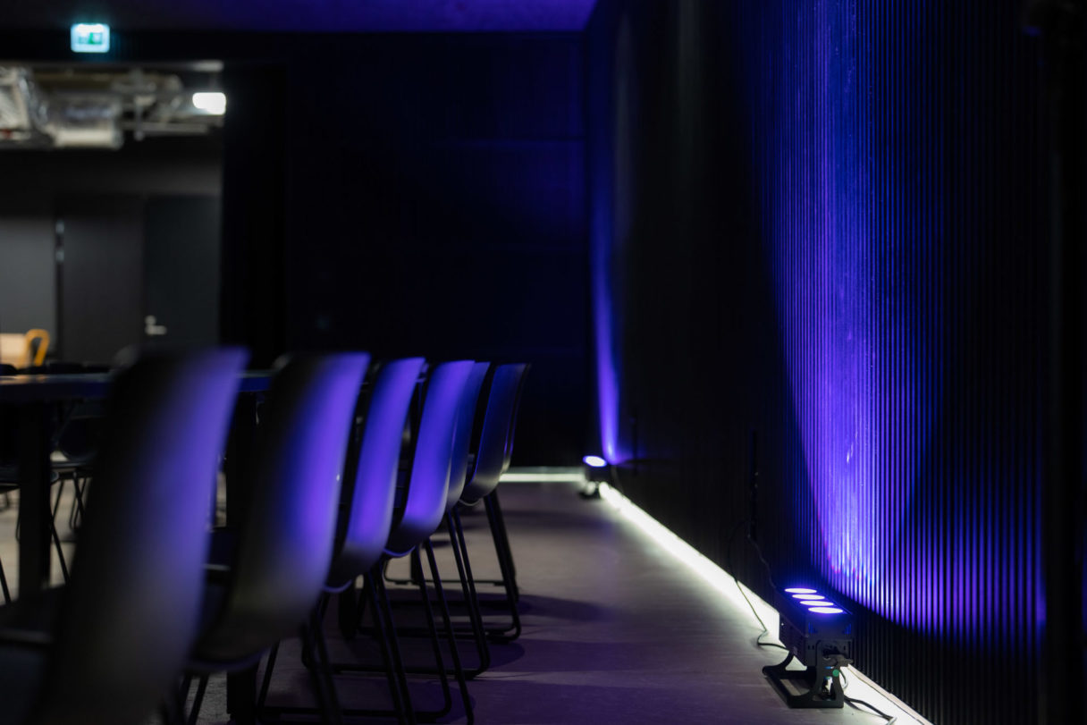 Tapahtumatilan tuolirivi ja seinää vasten hehkuva violetinsävyinen värivalaistus.