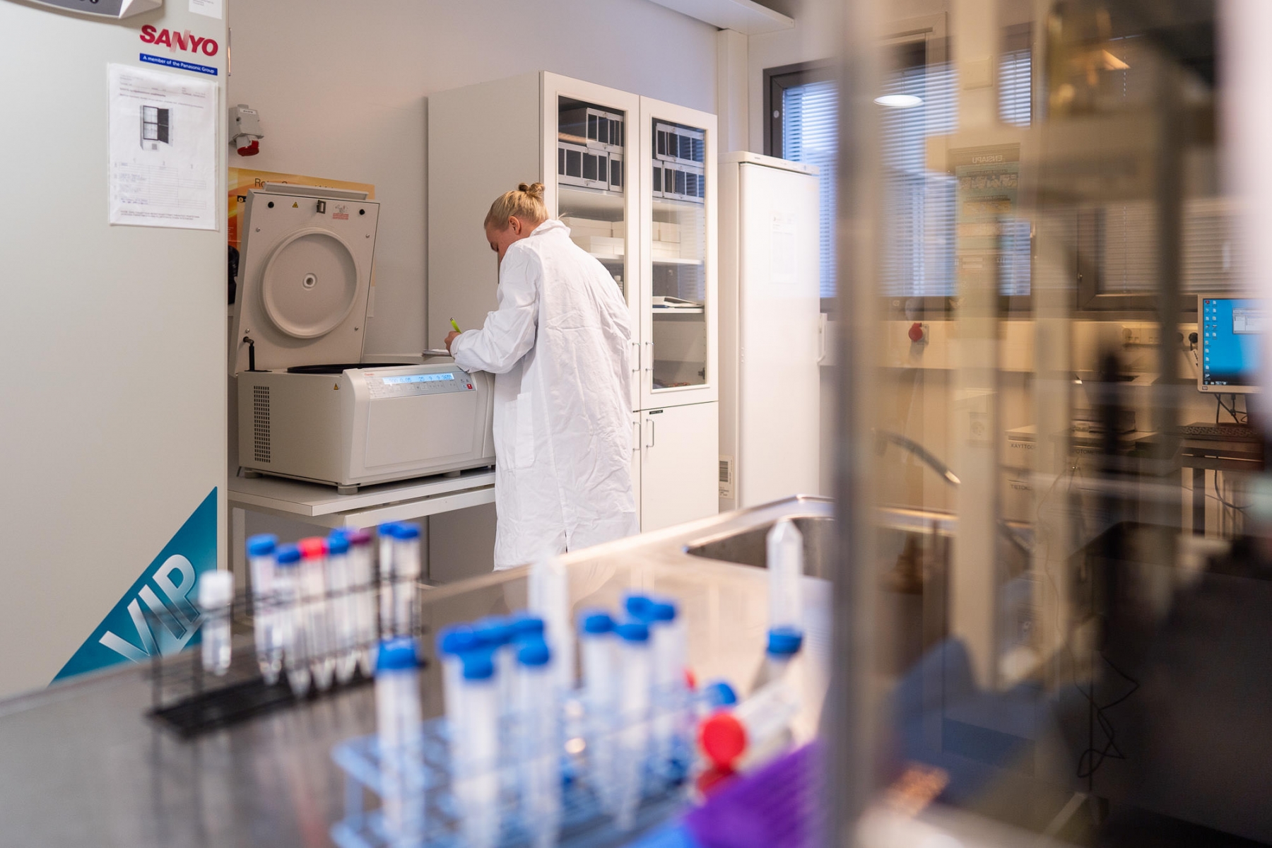 Laboratoriotila, jossa henkilö käyttää analyysilaitetta ja työpisteellä on reagenssiputkia ja laboratoriovälineitä.