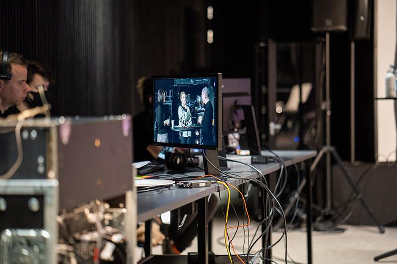 Tapahtumatekniikan ohjauspiste, jossa monitorilla näkyy live‑kuvaa ja pöydällä kulkee tuotannon kaapeleita ja laitteistoa