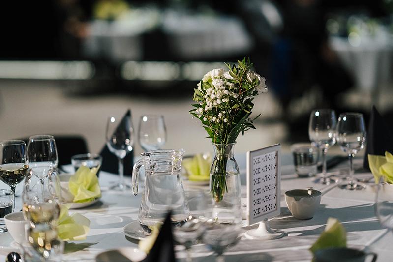 Juhlava pöytäkattauksen yksityiskohta, jossa on kukka-asetelma, vesikannu ja viinilasit valmiina tapahtumaillalliselle.