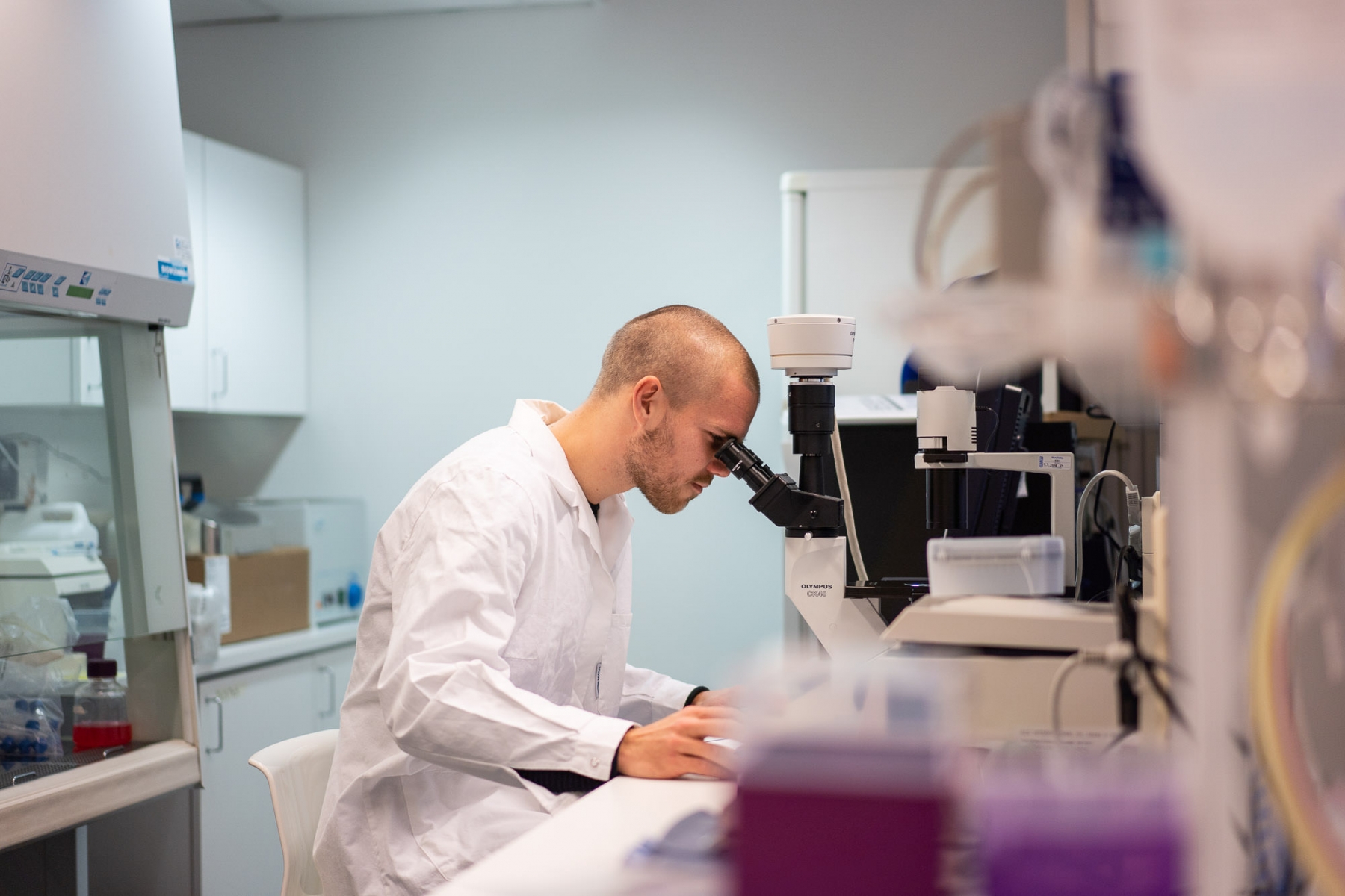 Henkilö tutkii näytteitä mikroskoopilla laboratoriossa tutkimuslaitteiden ympäröimänä.