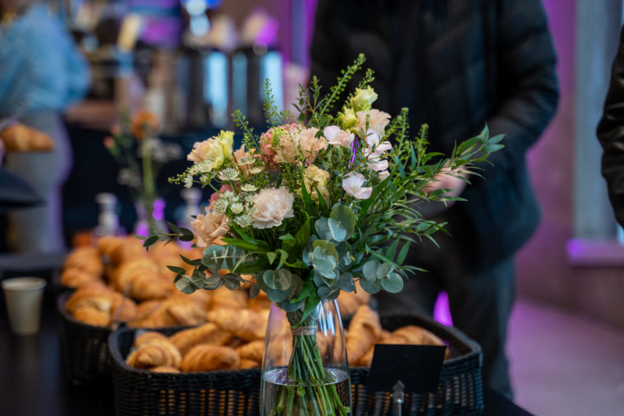 Kukkakimppu tarjoilupöydällä, jonka ympärillä on croissanteja ja kahvitarjoilu.