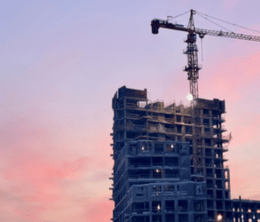 image d'illlustration d'article. Silhouette d'un immeuble en construction avec une grue. En arrière plan, le ciel dans des teintes roses violacées, pour évoquer un coucher de soleil ou une fin de journée